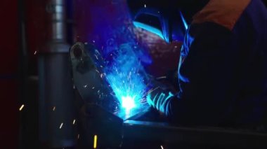 Fabrikada kaynak makinesiyle çalışan yetenekli bir metal işçisi güvenlik ekipmanı takıyor. El becerisi iş gücü kavramına göre metal imalatı ve inşaat bakım hizmeti