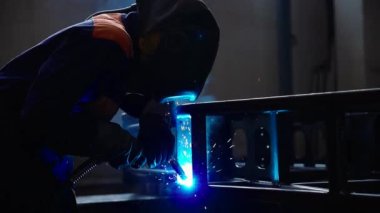 Fabrikada kaynak makinesiyle çalışan yetenekli bir metal işçisi güvenlik ekipmanı takıyor. El becerisi iş gücü kavramına göre metal imalatı ve inşaat bakım hizmeti