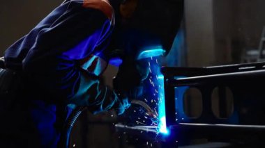 Fabrikada kaynak makinesiyle çalışan yetenekli bir metal işçisi güvenlik ekipmanı takıyor. El becerisi iş gücü kavramına göre metal imalatı ve inşaat bakım hizmeti