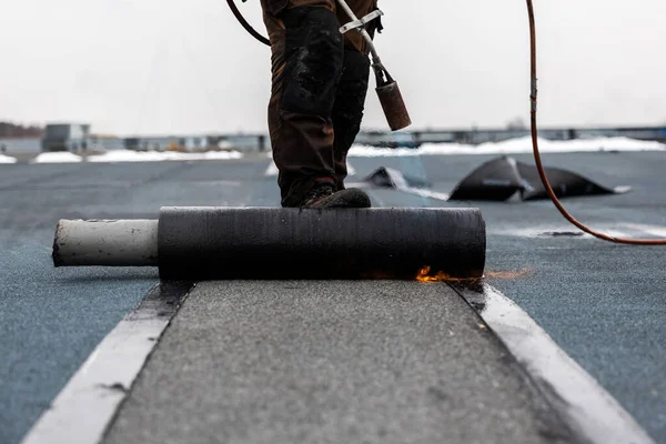 professional roofer at work securing rolled tar paper with a blowtorch on a flat roof installation process