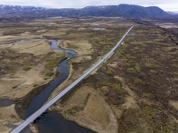 Sarmal nehirler ve geniş araziler üzerinden geçen uzun düz bir yolu olan İzlanda manzarası.