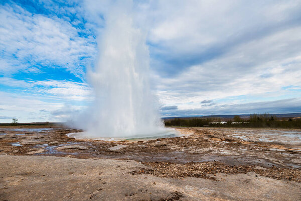 Strokkur geyser erupting in Iceland under a vibrant blue sky.