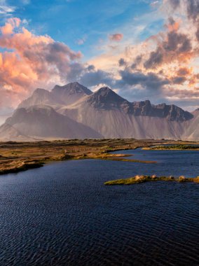 İzlanda 'da engebeli ve kayalık bir dağ sırasının nefes kesici panoramik manzarası. Açık mavi gökyüzü ve parlak güneş manzaranın enginliğini ve güzelliğini vurgular..