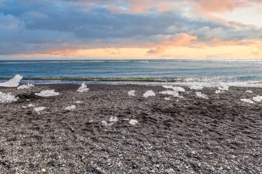 İzlanda 'da gün batımında Elmas Sahili' ndeki buzdağları canlı gökyüzü ve çakıl taşlarıyla