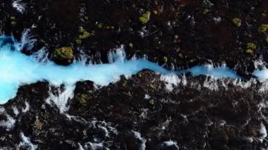 İzlanda 'daki volkanik arazide akan el değmemiş mavi nehrin havadan görünüşü İzlanda' nın doğal güzelliğini ve eşsiz jeolojik özelliklerini yakalıyor..