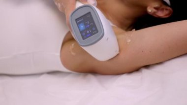 Profesyonel güzellik uzmanı bir güzellik salonunda bir kadının koltuk altını lazerle temizliyor.