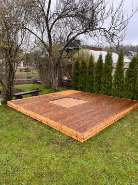 Çevresi yeşilliklerle çevrili bir arka bahçede merkezi kesilmiş ahşap bir güverte..