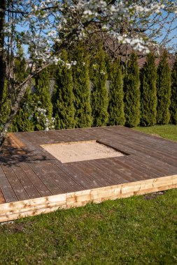 Güneşli arka bahçesinde merkezi bir kum havuzu olan ahşap güverte, temiz ve basit bir tasarım içeriyor.