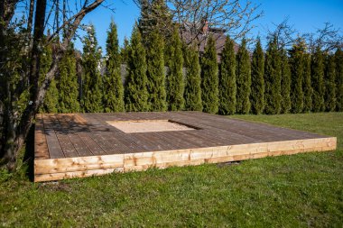 Güneşli arka bahçesinde merkezi bir kum havuzu olan ahşap güverte, temiz ve basit bir tasarım içeriyor.