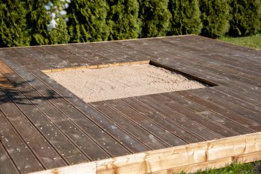 Güneşli arka bahçesinde merkezi bir kum havuzu olan ahşap güverte, temiz ve basit bir tasarım içeriyor.