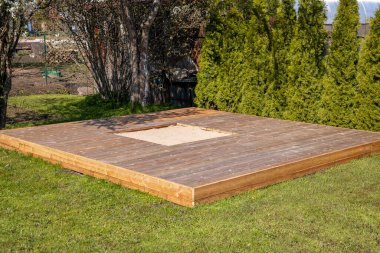 Güneşli arka bahçesinde merkezi bir kum havuzu olan ahşap güverte, temiz ve basit bir tasarım içeriyor.