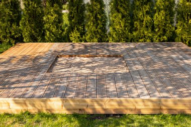 Ağaçlar ve doğal çevreyle çevrili, arka bahçesinde merkezi kum havuzu olan ahşap güverte.