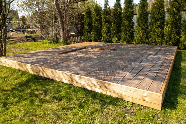 Ağaçlar ve doğal çevreyle çevrili, arka bahçesinde merkezi kum havuzu olan ahşap güverte.