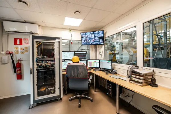 Makine işlemleri için canlı besleme ve sistem kontrollerini gösteren birden fazla monitörü olan bir endüstriyel tesiste kontrol odası.