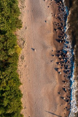 Kumsalın kıyısı, kumlu sahillere vuran dalgalar, suyun kenarına dağılmış kayalar.