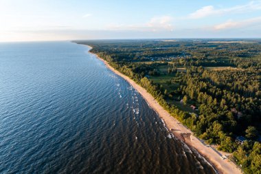 Letonya 'da Baltık Denizi' nin uzun bir kıyı şeridi, kumlu sahil berrak bir gökyüzü altında sakin mavi sularla buluşuyor.