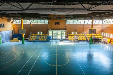 Basketbol sahasının içinde büyük bir salon salonu, yüksek tavanlar ve bol miktarda doğal ışık..