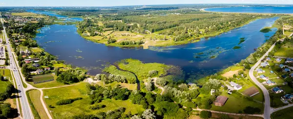 stock image Aerial view of Kekava, Latvia, highlighting a serene river meandering through lush fields and forests with a clear blue sky above.