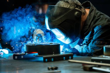 Close-up of a welder focused on his work, bright blue light and sparks emanating from the welding torch. clipart