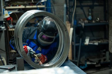 Welder skillfully working on a large metal ring, carefully welding joints in a well-equipped workshop. clipart