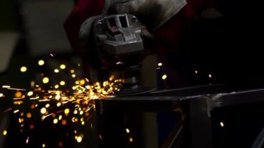 Bir işçi metal üzerinde kıvılcımlar saçan bir el değirmeni kullanır. Koruyucu eldivenler bu endüstriyel metal çalışma ortamında güvenliği vurguluyor.