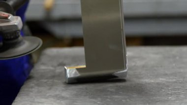 Bir işçi metal bir parçayı pürüzsüz hale getirmek için el bilgisayarı kullanır. Metal imalatına odaklanmış endüstriyel bir atölyede koruyucu eldivenler giyer..