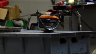Metal imalat atölyesinde siyah kasklı büyük bir tezgah bulunur. Matkap presi de dahil olmak üzere aletler ve ekipmanlar aktif metal işçiliği gösteriyor.