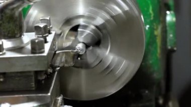 Bir metal torna makinası aktif olarak dönen bir iş parçası, metal talaşları üretiyor. Sağlam mekanizmada sürgüler ve yeşil boyalı bir bölüm var..