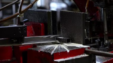 Kırmızı ve siyah bileşenleri olan metal kesme makinesi endüstriyel bir ortamda çalışır. Metal talaşı üretir ve soğutma sıvısını hassas bir iş için kullanır..