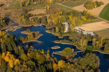 Hava manzaralı canlı bir sonbahar yeşilliği, bir gözlem kulesi ve dağınık binaları ve yolları olan kırsal bir arazide dönen bir su yolu yakalar..