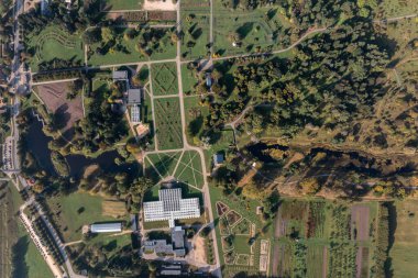 Merkezi bir seranın, geometrik bahçelerin, ağaç çizgili yolların ve sınırdaki bir su kütlesinin yer aldığı bir botanik bahçesinin hava perspektifi.