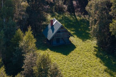 Dikenli yeşil çatısı ve kırmızı bacası olan ahşap bir kulübe sık ormanlarla çevrili yeşil bir düzlükte oturmaktadır. Güneş ışığı çimlerin üzerinde benekli gölgeler yaratır..