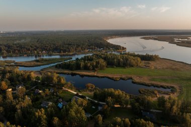 Dolambaçlı bir nehri, yemyeşil yemyeşil ve sık ormanları olan sakin bir manzara. Küçük ev kümeleri ağaçların arasında yuva yapar, altın ışıkla yıkanır..