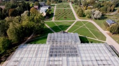 Simetrik yollar, yemyeşil yeşillikler ve kentsel zemin ile çevrili Geometrik Cam Sera Yapısı ile Şehir Botanik Bahçesi.