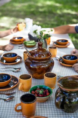 Güneşli bir yaz gününde bahçesinde güzel toprak eşyalar olan bir masa.