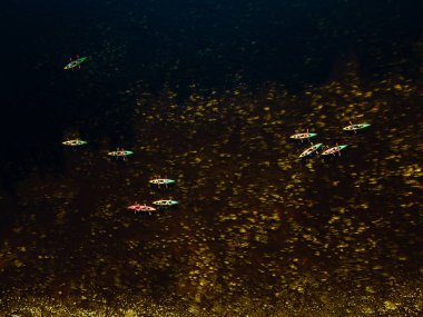 Bir grup renkli kano, etrafını çevreleyen yemyeşil bir su nehrinde sıralanmış.