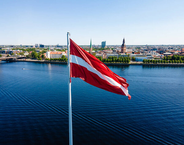 Huge Latvian flag flutters in the wind with Riga old town in the background in Latvia. Beautiful summer day.