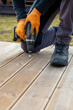 Güverte ya da teras inşaatı, elektrikli tornavidayla inşaatçı eli hamile bırakılmış tahtaları kuruyor.