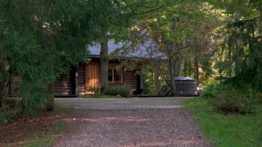 Mavi metal çatılı ahşap bir kulübe yeşil yapraklı ağaçların arasına kurulmuştur. Kabine giden asfalt bir yol var, sağ tarafta da jakuzi var..