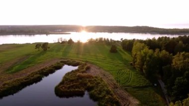 Gün batımında sakin bir manzara, sakin bir nehir ya da göl, suya yansıyan ılık güneş ışığı ve yemyeşil bir gölet içerir..