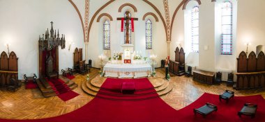 Katedralin içinde mumlar ve çiçeklerle çevrili süslü bir sunağın üzerinde büyük bir haç bulunur. Uzun camlı pencereler boşluğu aydınlatır.