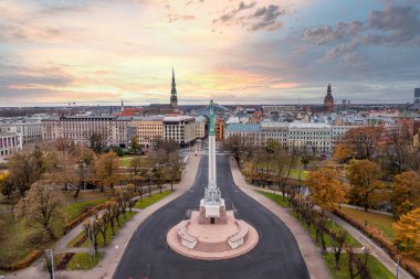 Özgürlük Anıtı, Letonya Riga 'da sonbahar yaprakları arasında duruyor. Gökyüzünün altında St. Peter Kilisesi ve Riga Katedrali yer almaktadır..
