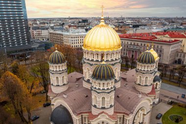 Riga, Letonya 'daki İsa' nın Doğuşu Katedrali 'nde, şehir manzarası ve günbatımında modern yüksek binalarla çevrili altın kubbeler ve karmaşık ayrıntılar yer alıyor..