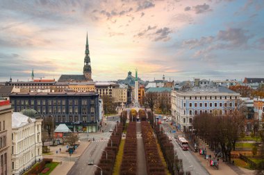 Riga, Letonya 'nın havadan görünüşü, Aziz Peter Kilisesi kulesi, tarihi ve modern binalar, ve günbatımı gökyüzünün altında uzanan bir ağaç bulvarı..