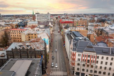 Riga, Letonya 'nın havadan görünüşü, değişik mimariye sahip canlı bir şehir manzarası. Sıcak bir günbatımı gökyüzüne karşı yükselen yeşil bir kilise kulesi.