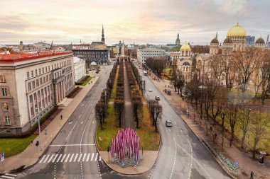 Aerial view of Riga, Latvia, showcasing the Nativity of Christ Cathedral's golden domes, tree lined central avenue, and modern art installation in the foreground. clipart