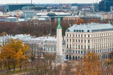 Riga, Letonya 'nın havadan görünüşü, tarihi ve modern mimarinin ortasındaki Özgürlük Anıtı' nı ön plana çıkarıyor ve arka planda güz ağaçları bulunuyor..