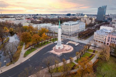Riga, Letonya 'nın havadan görünüşü, dairesel bir plaza ve sonbahar ağaçları arasındaki Özgürlük Anıtı' nı vurguluyor. Şehir manzarası çeşitli mimariye sahiptir..