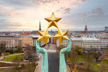 Letonya Riga 'daki Özgürlük Anıtı üç yıldızlı bir figürle dimdik ayakta duruyor. Şehir manzarasında, Aziz Peter Kilisesi de dahil olmak üzere tarihi ve modern mimari yer alıyor..