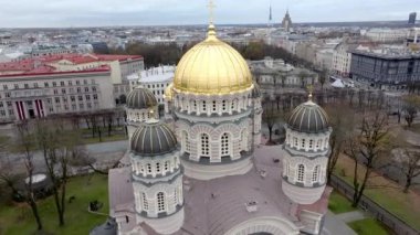 Riga, Letonya 'daki İsa' nın Doğumu Katedrali 'nde arka planda Riga TV Kulesi ve ağaçlarla kaplı caddelerin bulunduğu şehir manzarası arasında altın bir kubbe yer alıyor..